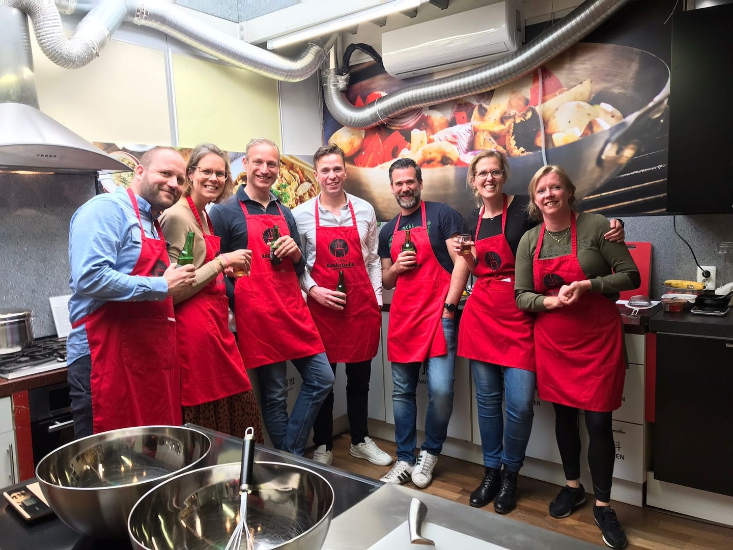 Groep vrienden in rode schorten met een drankje in de keuken